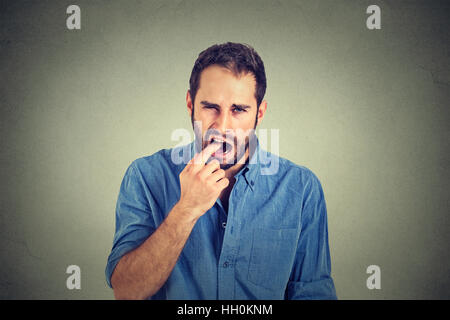 angewidert Mann mit Finger im Mund unzufrieden mit Lage Service bereit, werfen sich auf graue Wand Hintergrund isoliert. Menschlichen Gesichtsausdruck, emotio Stockfoto