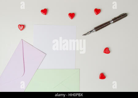 Umschläge, Nachricht, Stift und kleinen roten Herzen auf weißen Tisch. Liebesbrief, Valentinstag-Konzept Stockfoto