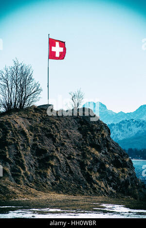 Schweizer Flagge, die über einen Berg in den Alpen mit leichten Winterschnee bedeckt an einem kalten sonnigen blauen Himmel Tag Stockfoto