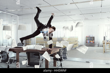 Fröhliche Jungunternehmer tanzen in seinem Büro. Mixed-media Stockfoto