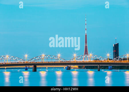 Riga, Lettland. Zwei Brücken über die Daugava zusammen: Stein Akmens und Eisenbahnbrücke In Abend-Beleuchtung mit roten Radio TV Tower Hintergrund im Sommer Stockfoto