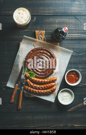 Gegrillte Würstchen und dunkles Bier über verbrannten Holz Hintergrund Stockfoto