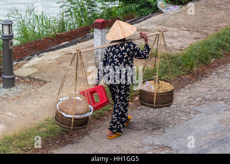 Eine Straße Verkäufer tragen ihre waren in zwei Körben aufgehängt eine Schulterpasse. Auf dem Parfüm-Fluss, Hue, Vietnam übernommen. Stockfoto