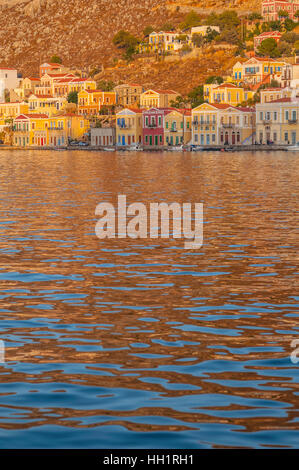 Gebäude auf dem Hügel mit Blick auf den Hafen auf Symi Griechenland bei Sonnenuntergang Stockfoto