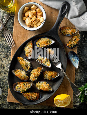 Lecker gebackene Muscheln auf einer eisernen Pfanne mit Paniermehl, Zitrone, Petersilie, Knoblauch und Olivenöl. Stockfoto