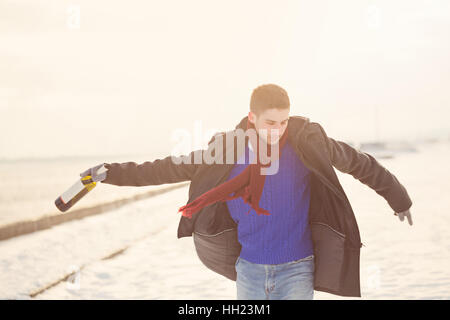 Mann geht mit einer Flasche Wein. Er ist im Wintermantel, Schal und Handschuhe angezogen. Mann war betrunken. In den Hintergrund, den Schnee und den Sonnenuntergang. Stockfoto