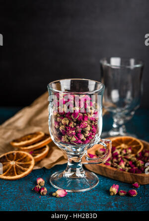 Trockenen Teerose Knospen in einem Glas auf dunkelblauem Hintergrund Stockfoto