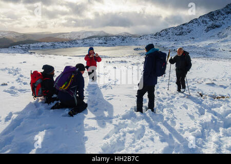 Wanderer für ein Foto in Schnee posiert von Llyn y-Foel mit Moel Siabod Daear Ddu East Ridge in Snowdonia. North Wales, Großbritannien, Großbritannien Stockfoto