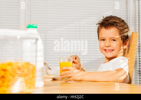 Fröhlicher Junge trinkt Orangensaft beim Frühstück Stockfoto