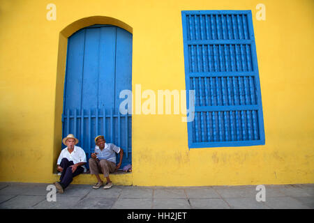 Zwei Männer sitzen vor einer typischen bunten Wand eines Hauses in Santiago De Cuba mit einer Cohiba Zigarre Stockfoto