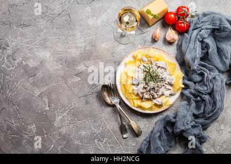 Frische Tagliatelle Pasta mit Pilzen in Rahmsoße in weißer Teller auf grauem Hintergrund, Ansicht von oben mit Textfreiraum Stockfoto