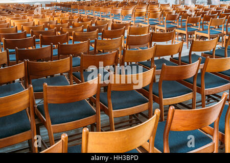 Viele leere die gleichen Holzstühlen mit Rückenlehne und blaue Polster In ordentlichen Reihen im großen Saal stehen. Stockfoto