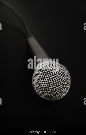 Schwarz und Silber Gesangsmikrofon mit Kabel erhöhte Ansicht hautnah in Dunkelheit, auf schwarzem Hintergrund, persönlichen Perspektive Stockfoto