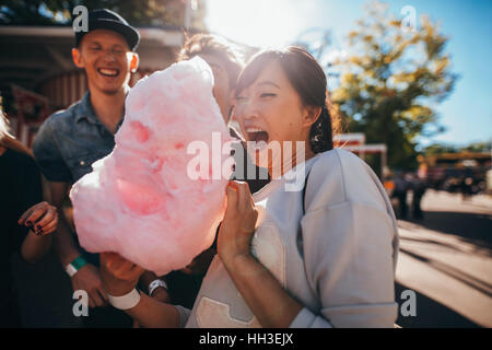 Glückliche junge Freunde Zuckerwatte im Freien zu essen. Junge Menschen und Frauen mit Baumwolle Zuckerwatte am Festplatz. Stockfoto