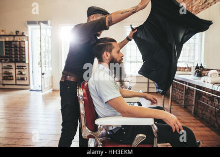 Barbier, legen Sie ein Blatt zur Deckung seines Mandanten vom Haare schneiden. Männliche Friseur bei der Arbeit mit schöner Mann auf Stuhl sitzend. Stockfoto