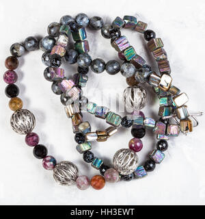 verworrenen Halskette aus Regenbogen Pyrit natürliche Kristalle, Turmalin und Achat Kugeln, Silber und Perlmutt Perlen auf Betonplatte Stockfoto