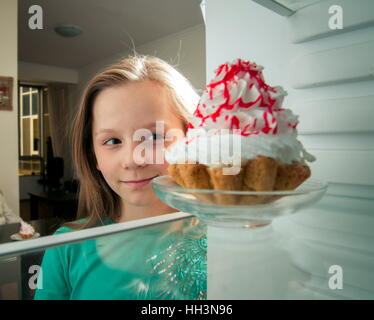 Mädchen sieht die süßen Kuchen in den Kühlschrank stellen Stockfoto