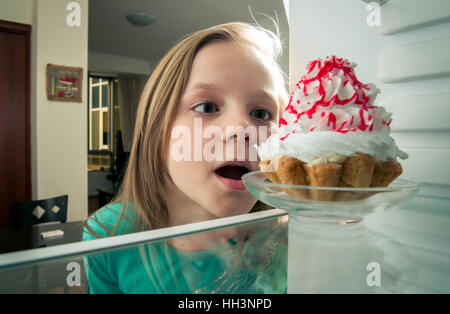 Mädchen sieht die süßen Kuchen in den Kühlschrank stellen Stockfoto