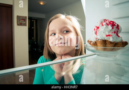 Mädchen sieht die süßen Kuchen in den Kühlschrank stellen Stockfoto