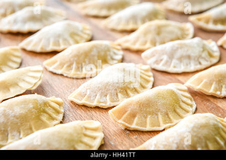 Herstellung von hausgemachten Knödel Teig Tortellini oder Ravioli. Modell für hausgemachte Pasta mit Fleisch gefüllt. Bio Zubereitung auf einem Schreibtisch aus Holz. Stockfoto