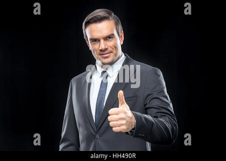 Gut aussehend Geschäftsmann im Anzug zeigen Daumen und lächelt in die Kamera Stockfoto
