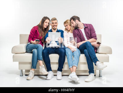 Interessierte junge Freunde Geräte verwenden und mit Blick auf digital-Tablette auf couch Stockfoto