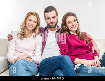 Junge Freunde sitzen auf Couch umarmt und Blick in die Kamera Lächeln Stockfoto