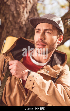 Junge bärtige Mann Reisenden mit Rucksack unter riesigen Baum stehen Stockfoto