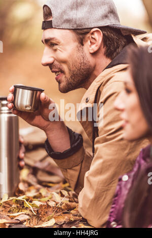 Seitenansicht der hübsche junge Mann sitzt in der Nähe von Brünette Frau und halten Tasse aus Thermoskanne mit Heißgetränk Stockfoto