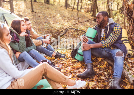 Junge Freunde Reisende sitzen und reden in der Nähe von Zelt im herbstlichen Wald Stockfoto