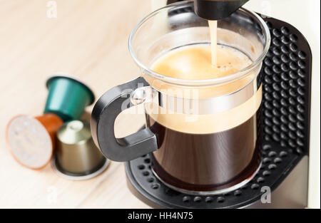 Single-Portion Kaffee aus dem Automaten verzichtet Espresso in einer Glasschale mit Kaffee-Kapseln im Hintergrund Stockfoto