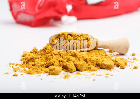 Aromatische gelbe Farbe Currypulver Zutat auf weißen Tisch mit hölzernen Schaufel und rotem Stofftasche im Hintergrund Stockfoto