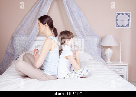 Glückliche Mutter und Tochter zu meditieren und Lächeln während der Sitzung in Yoga-Pose auf dem Bett zu Hause. Studio gedreht. Stockfoto