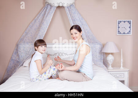 Glückliche Mutter und Tochter zu meditieren und Lächeln während der Sitzung in Yoga-Pose auf dem Bett zu Hause. Studio gedreht. Stockfoto