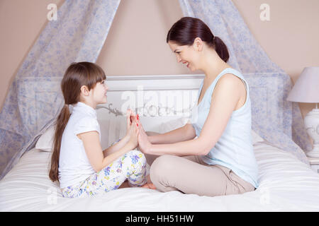 Glückliche Mutter und Tochter zu meditieren und Lächeln während der Sitzung in Yoga-Pose auf dem Bett zu Hause. Studio gedreht. Stockfoto