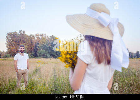 Schöne Frau holding Bouquet von gelben Blüten und Blick in die Kamera mit ihrem Freund auf Hintergrund. Stockfoto