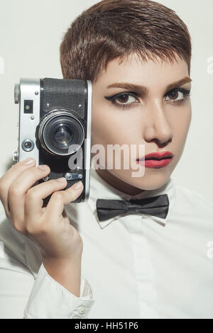 junge schöne Fotografin Frau mit kurzen Haarstil und klassische Verschleiß mit Fliege. Kamera halten und auf der Suche. Stockfoto