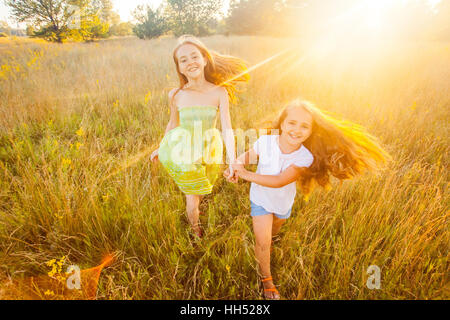Zwei schöne Schwestern laufen auf dem Rasen im Naturpark im Freien im Sommer. Freiheit und unbeschwert. Glückliche Kindheit. Stockfoto