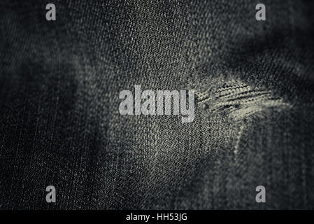 Wort und faded Denim Jean Material mit einem ausgefransten Loch in einer horizontalen Komposition in schwarz und weiß mit abgenutzten Material. Stockfoto
