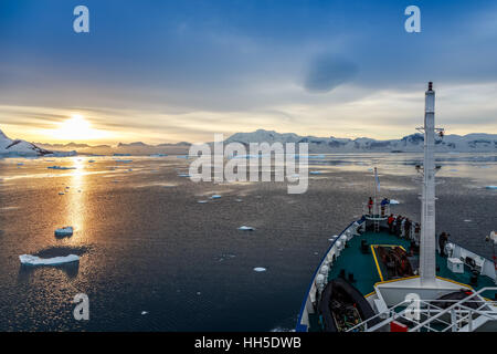 Blick auf den Sonnenuntergang und die Menschen versammelten sich auf dem Deck, Eisberge driften bei Lemaire-Kanal, Antarktis Stockfoto