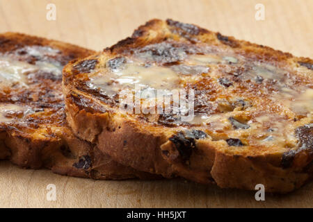 Nahaufnahme von zwei Scheiben geröstetes Johannisbeere Brot mit Schmelzen von Butter auf einem Holzbrett, erschossen in natürlichem Licht mit flachen DoF Stockfoto