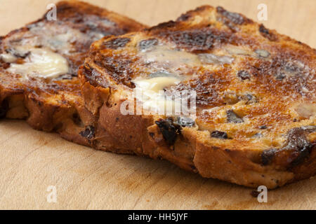 Nahaufnahme von zwei Scheiben geröstetes Johannisbeere Brot mit Schmelzen von Butter auf einem Holzbrett, erschossen in natürlichem Licht mit flachen DoF Stockfoto