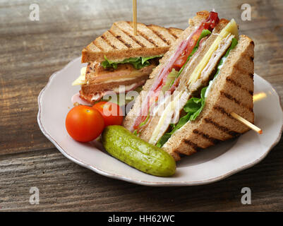 Foto von einem Club-Sandwich mit Türkei, Speck, Schinken, Tomaten, Käse, Salat, und garniert mit einer Essiggurke und zwei Kirschtomaten. Stockfoto