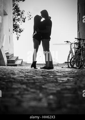 Foto von einer jungen Frau und Mann, umarmen und küssen in einer Gasse.  Leichte Maserung sichtbar. Stockfoto