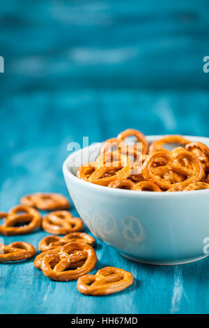 Salzige Snacks Mini Brezeln in Schüssel auf blauen Holztisch Stockfoto