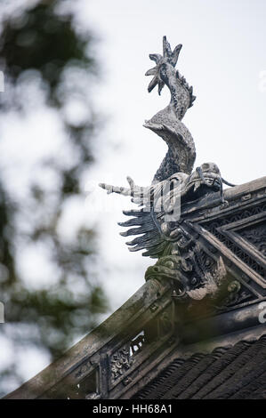Traditionelle Drachen auf einem Garten Dach. Shanghai, China. Dekorative Skulptur einer mythischen Kreatur auf einem alten Gebäude, Bäume sichtbar unscharf Stockfoto