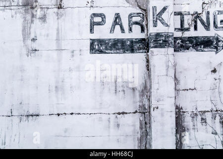 Detail von der Seite eines alten Gebäudes wo das Wort Parkplatz in schwarz mit einem schwarzen Pfeil rechts gemalt worden ist Stockfoto