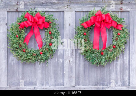 zwei helle und festliche Weihnachtskränze hängen nebeneinander, ein Scheunentor Stockfoto