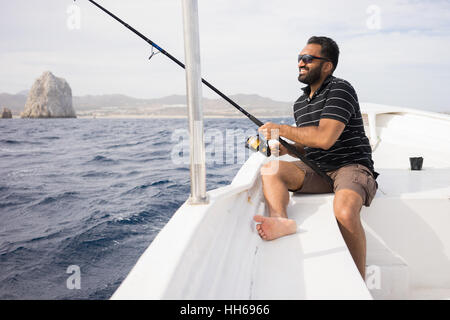 Ostasiatische junge Mann auf dem offenen Wasser vom Boot aus Angeln. Schönen sonnigen Tag mit der Küste im Hintergrund sichtbar. Stockfoto