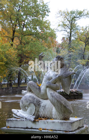 Eine graue und weiße Marmorstatue von Cupido reitet auf einem Delphin. Die Statue ist Teil der Sun-Brunnen im Hintergrund zu sehen. Stockfoto